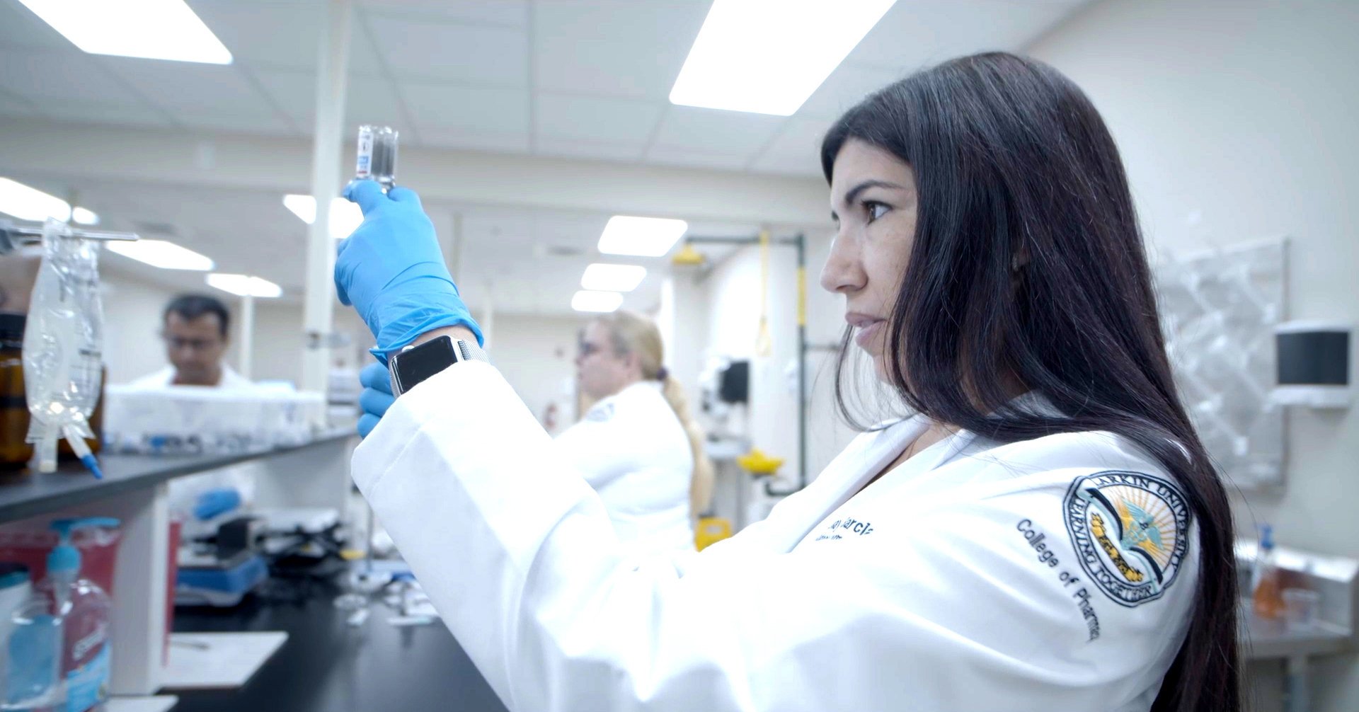 Pharmacy student in lab coat examining vial in a laboratory at Larkin University College of Pharmacy.